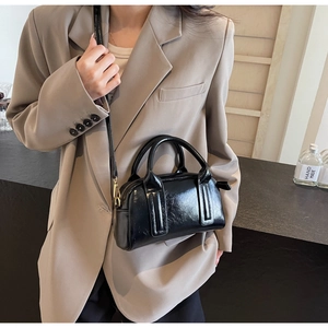 Dettaglio di borsa Boston nera con finiture dorate indossata su un blazer beige