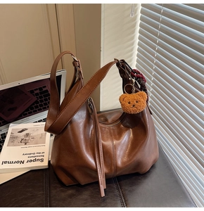 Detail of dark brown leather hobo bag with teddy charm and silk scarf decoration