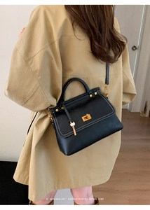 Detail of black leather handbag with golden twist lock and white contrast stitching