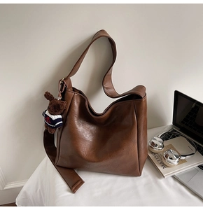 Détail du sac seau mat marron foncé avec large bandoulière, ours en peluche et livre d'art