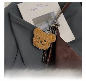 Close-up of a khaki plush bear charm with silver metal clasp on a leather bag strap