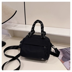 Detail of black nylon crossbody bag with striped rope handle and silver logo badge
