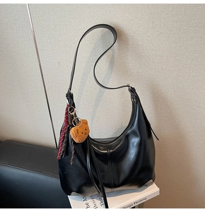 Detail of glossy black crescent shoulder bag with plush bear charm and woven cord