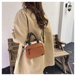 Brown corduroy crossbody bag with woven handles shown in a vintage outdoor setting