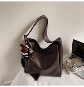 Détail du sac seau en cuir mat marron foncé avec breloque ours et essentiels de bureau