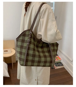 Detail of green and brown plaid tote bag with leather shoulder strap worn by model