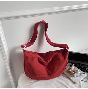 Detail of deep red crescent crossbody bag with adjustable strap and smooth nylon texture