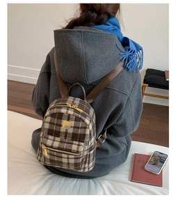Detail of a brown plaid mini backpack with golden metal accents worn by a model