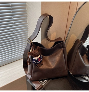 Détail du sac seau en cuir mat marron foncé avec breloque ours et large bandoulière