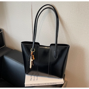 Dettaglio di una borsa tote nera lucida con spalline sottili e nappa decorativa in perline