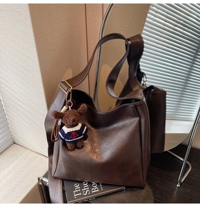 Détail d'un sac seau en cuir souple marron foncé avec un charmant ours en peluche