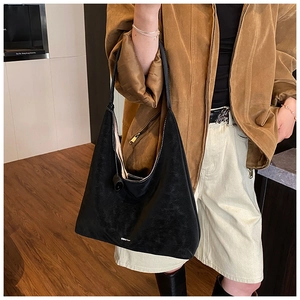 Detail of black suede large tote bag with integrated wide strap and spherical charm pendant