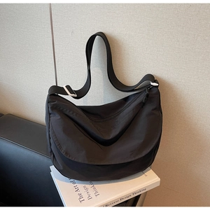 Detail of black nylon dumpling bag with adjustable strap leaning against a textured wall