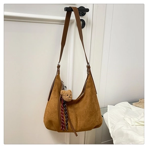 Detail of brown suede hobo bag with plush bear charm and striped ribbon on door handle