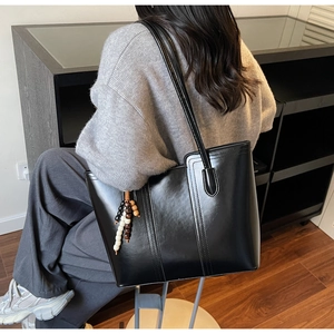 Dettaglio borsa tote in PU nero lucido con cuciture e ciondolo di perline boho