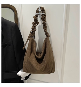 Detail of soft brown suede hobo bag with unique ruched strap hanging on a wall hook