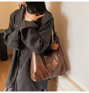 Brown large faux leather tote bag with plush bear charm and ribbon on model's shoulder