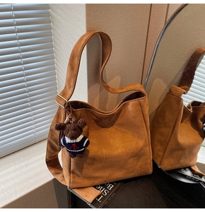 Détail du sac seau en daim marron avec bandoulière réglable et breloque ours décorative