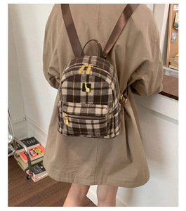 Detail of brown plaid texture and golden zipper on wool blend backpack shown on model