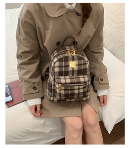 Detailed close-up of brown plaid backpack showing woolen fabric and gold hardware logo