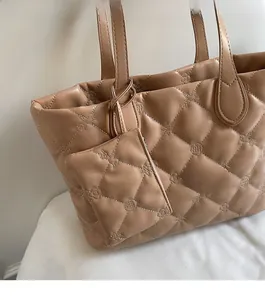 Close-up of quilted rhombic pattern and round floral embossed logo on camel tote bag