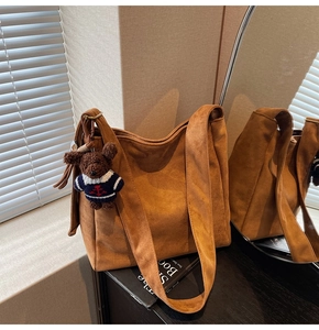Détail d'un sac seau en daim marron avec un pendentif ours dans un reflet chaleureux