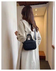 Rear view of a black contrast-stitch crossbody bag with woven handle on a model
