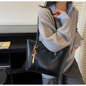 Dettaglio di una borsa tote nera capiente con ciondolo decorativo in perle di legno sulla tracolla
