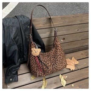 Close-up of leopard print canvas hobo bag with leather strap and plush bear charm on a bench