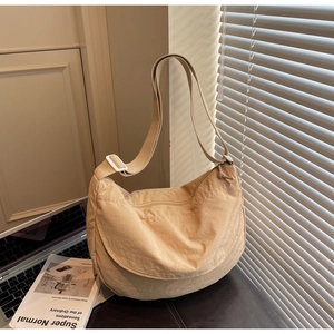 Detail view of beige nylon crescent bag with adjustable strap on desk near books