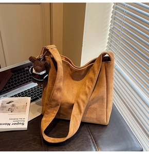 Détail du sac seau en daim marron avec une large bandoulière et un pendentif ours