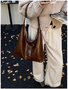 Detail of a brown leather hobo tote bag featuring white logo and chic autumn outfit styling