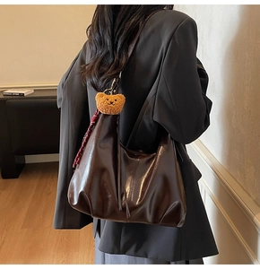 Detail of a large vintage brown glossy leather tote bag with a cute plush bear and scarf