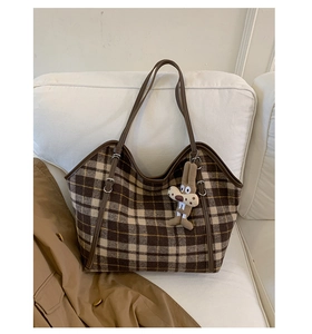 Detail of a plaid tote bag in wool fabric with leather handles and a plush bunny charm