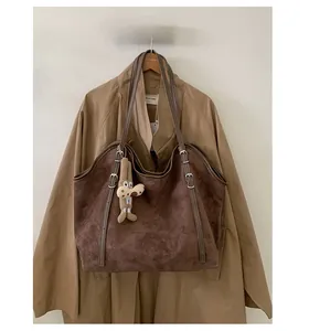 Detail of dark brown suede tote bag with plush puppy charm and long leather strap
