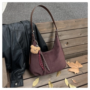 Close-up of deep burgundy suede hobo bag on a wooden bench with autumn leaves detail