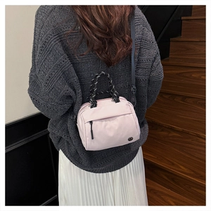 Pink nylon crossbody bag with woven handles and front pocket shown in lifestyle setting