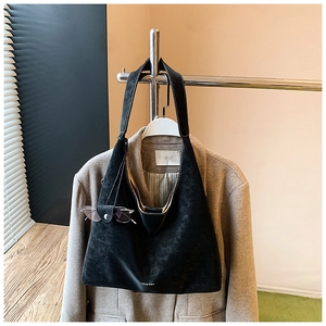 Detail of a large black suede tote bag hanging on a rack with a brown wool coat