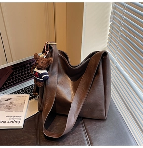 Détail d'un sac seau marron mat avec porte-clé ours en peluche et ombres douces