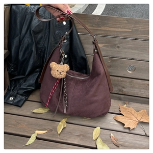Detail of dark brown matte leather hobo bag with a cute bear charm on a wooden bench