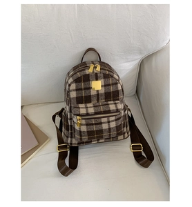 Close-up of brown plaid wool backpack with golden zippers on a white sofa background