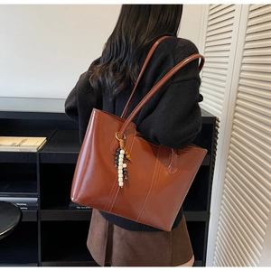 Brown faux leather tote bag with wooden bead charm shown in a lifestyle shoulder carry