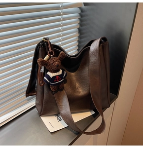 Détail du sac seau marron foncé avec bandoulière large et un charmant petit ours en peluche