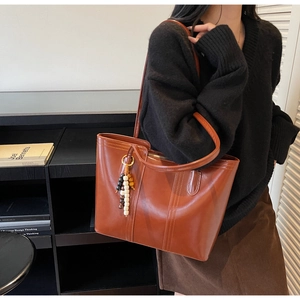 Dettaglio di una borsa tote in pelle marrone scuro con ciondolo a nappa in perline colorate