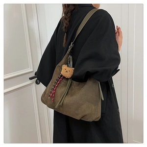 Detail of olive green suede hobo bag with teddy bear charm and leather tassel decoration