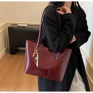Vista laterale della grande borsa tote bordeaux con ciondolo di perline indossata dal modello