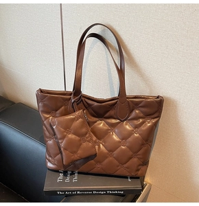 Detail view of a brown quilted tote bag with a matching mini pouch on a black sofa