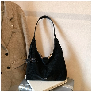 Close-up of black suede hobo bag with logo detail on a silver suitcase and books