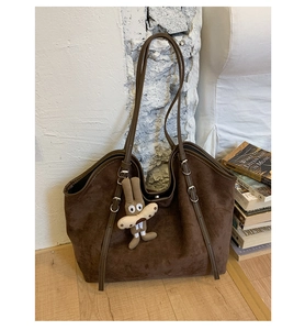 Detail of a large brown suede tote bag with slim straps and a cute plush dog pendant