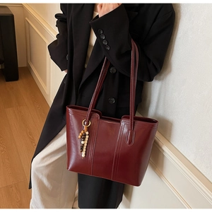 Vista dettagliata della borsa tote bordeaux con ciondolo in legno e finitura in pelle